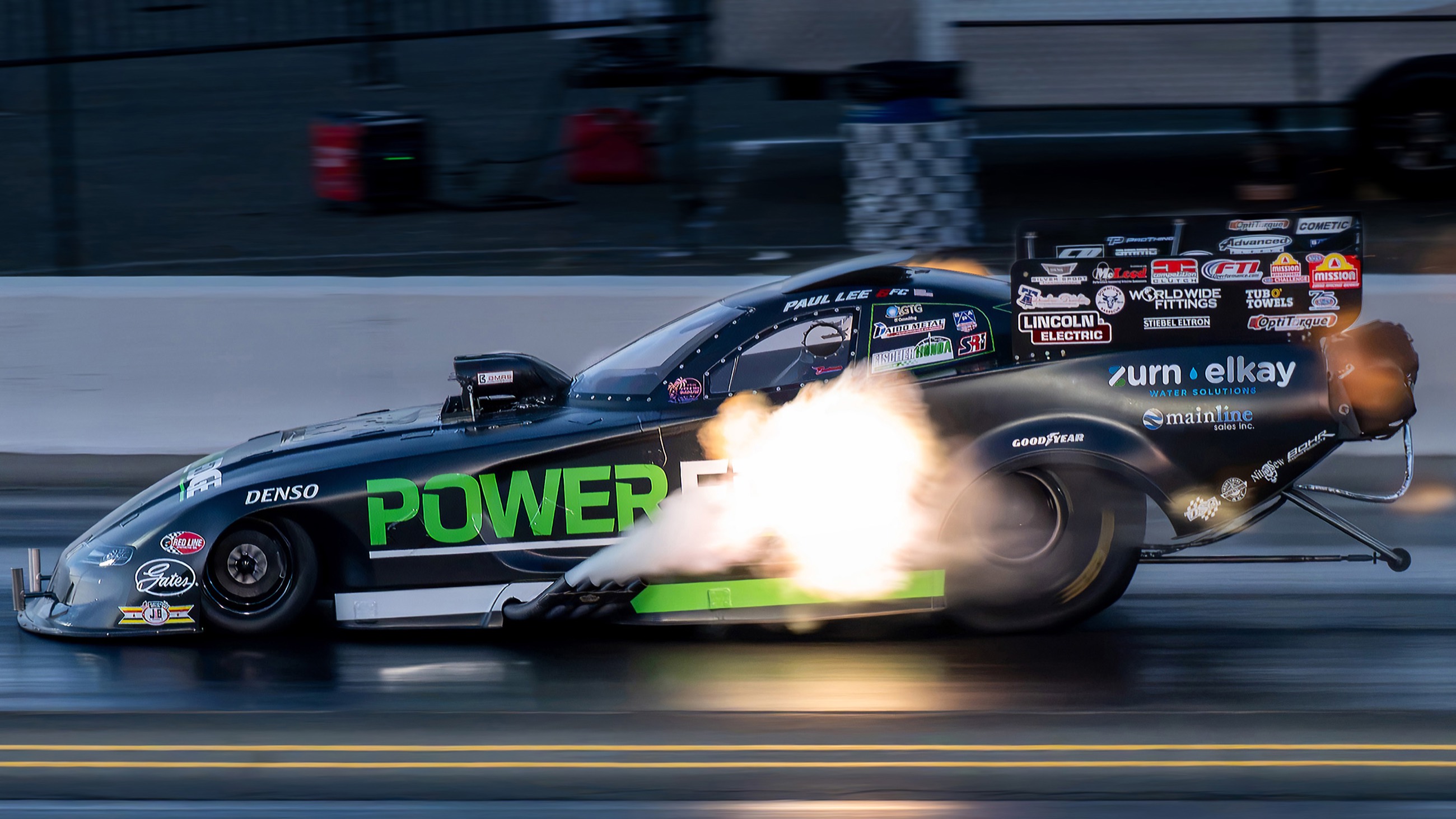A funny car at dusk erupting in a fireball from the exhaust headers under full power.
