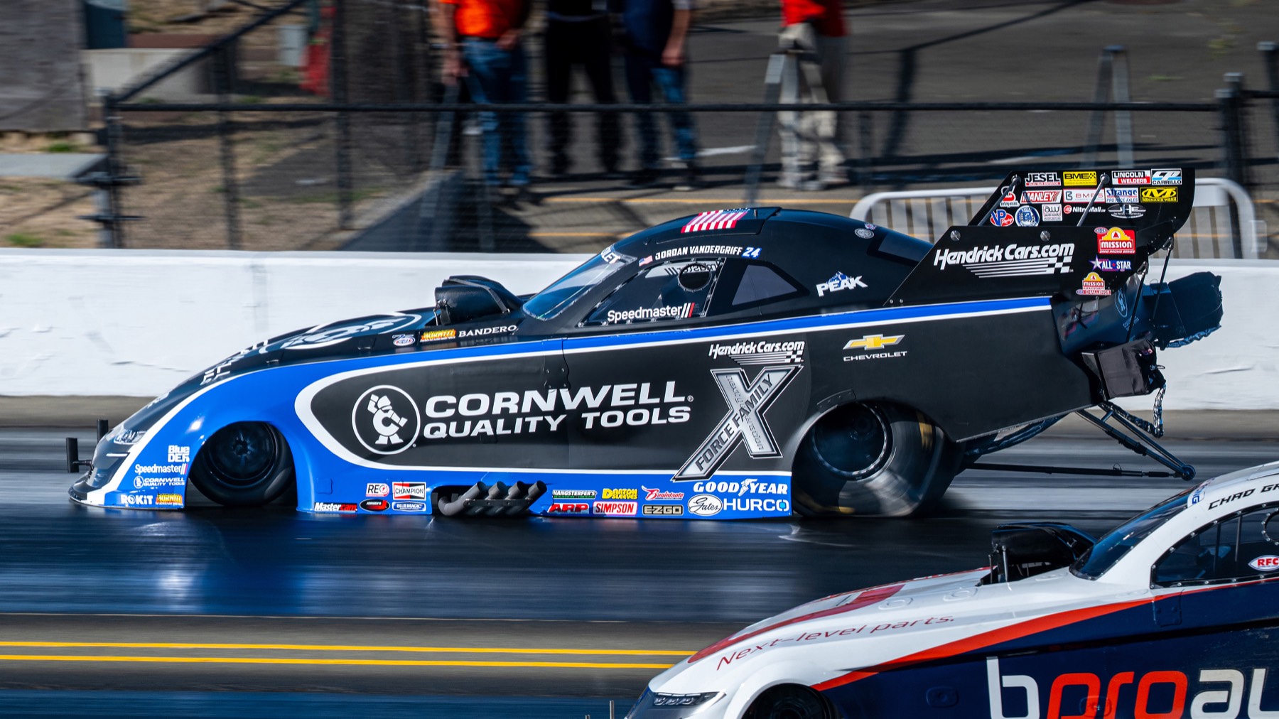 A blue funny car mid-run, clutch dust drifting behind the rear tires.