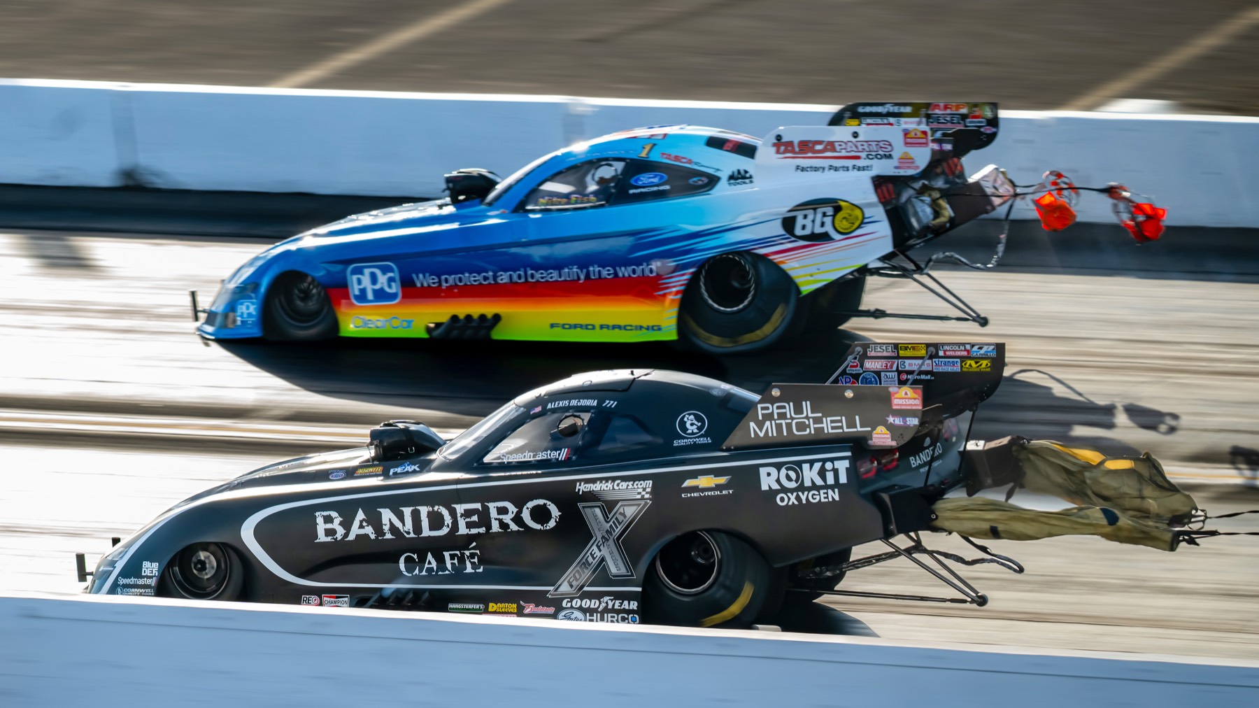 A rainbow funny car and a black funny car close together near the finish line.