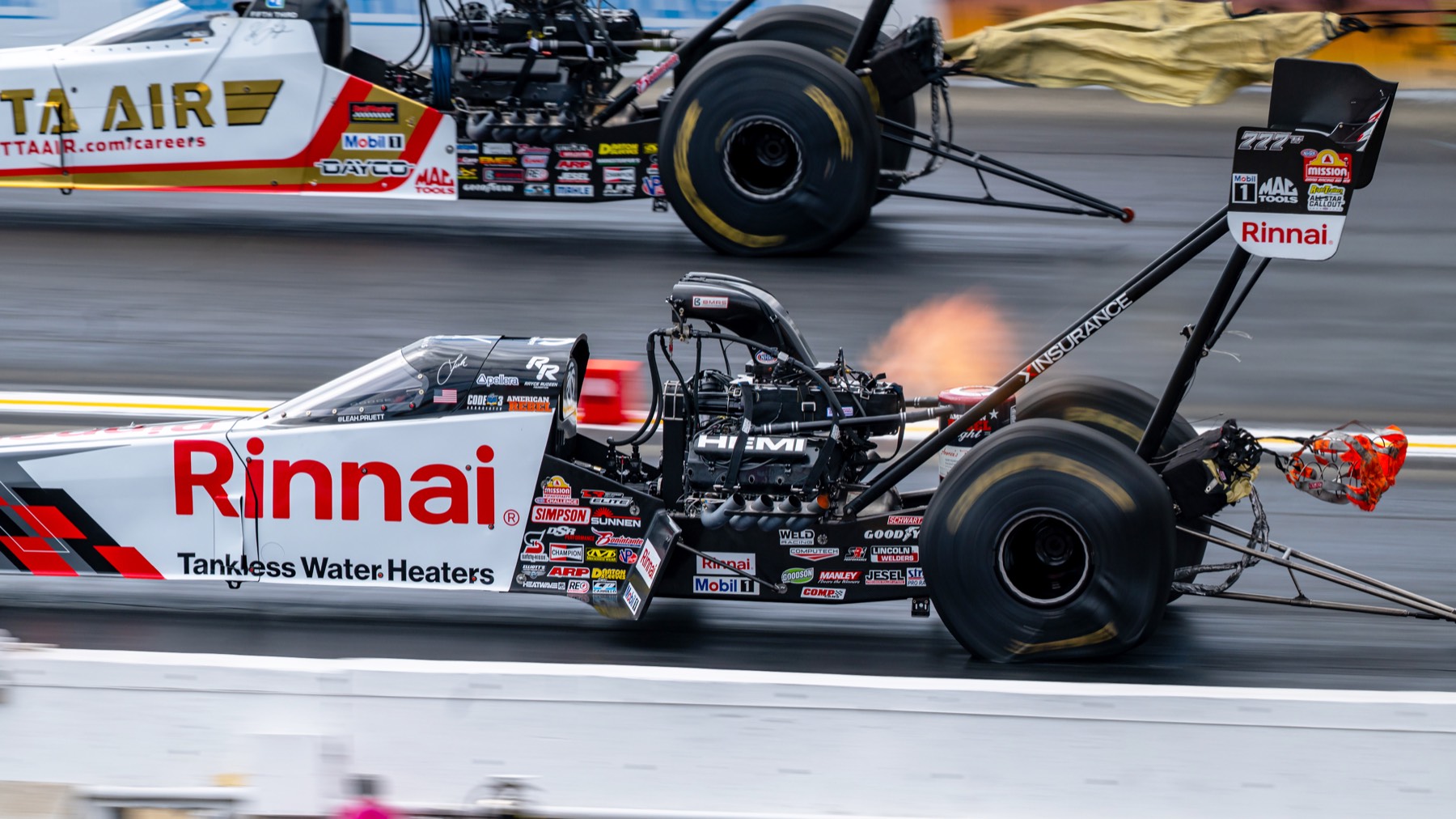 Two top fuel dragsters at launch, flames visible, front ends stretching forward.